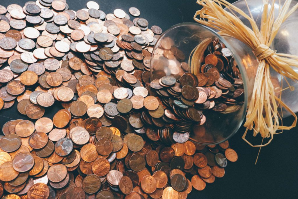 A glass jar tipped over and spilling a puddle of pennies. Montessori preschool.